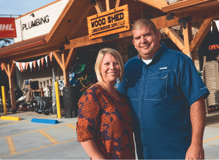 A man and woman standing in front of a lumber supply shop