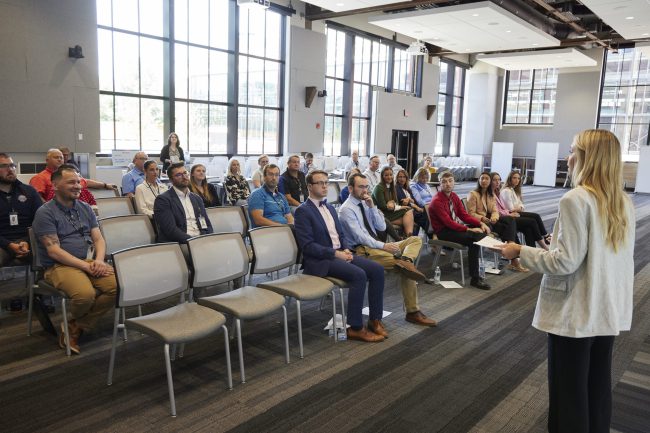 Do it Best intern in professional dress presenting in front of other interns and staff members in large conference room