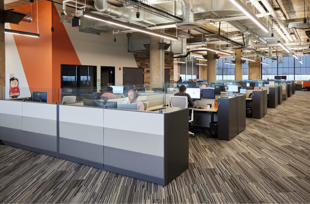 Employee working in open office space with low cubicle walls and striped carpet